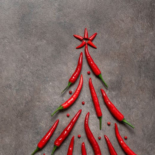 Red chili peppers arranged in the shape of a Christmas tree on a dark surface